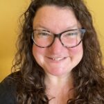 Ariadne Cass-Maran is smiling, with long curly hair and glasses against a yellow background