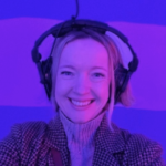 A picture of Suzanne smiling looking at the camera and  wearing headphones 